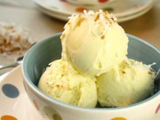 Three scoops of coconut ice cream in a bowl topped with toasted shredded coconut