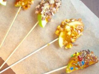 apple slices on sticks coated in caramel and chopped candy