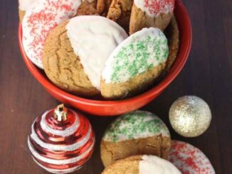 Molasses Spice Cookies in a read bowl on a dark cutting board with a red Christmas tree ornament